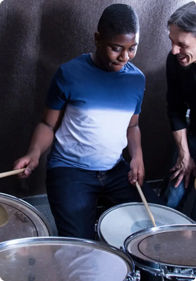 Teen learning to play drums with instructor guidance in a music class setting.
