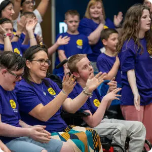 Group clapping and enjoying a lively event, all wearing matching purple t-shirts with yellow badges.