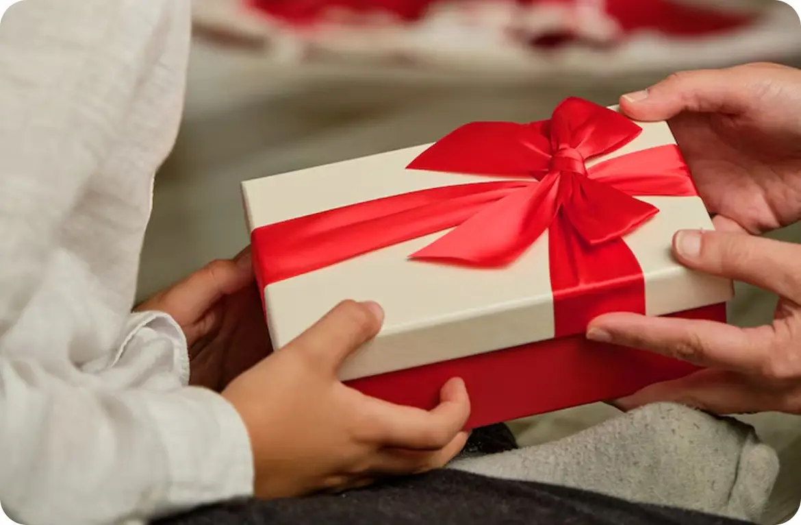 Hands exchanging a gift box wrapped in red ribbon, symbolizing celebration and joy.