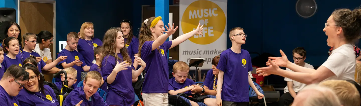 Group of enthusiastic young people with disabilities participating in a music session, wearing purple shirts.
