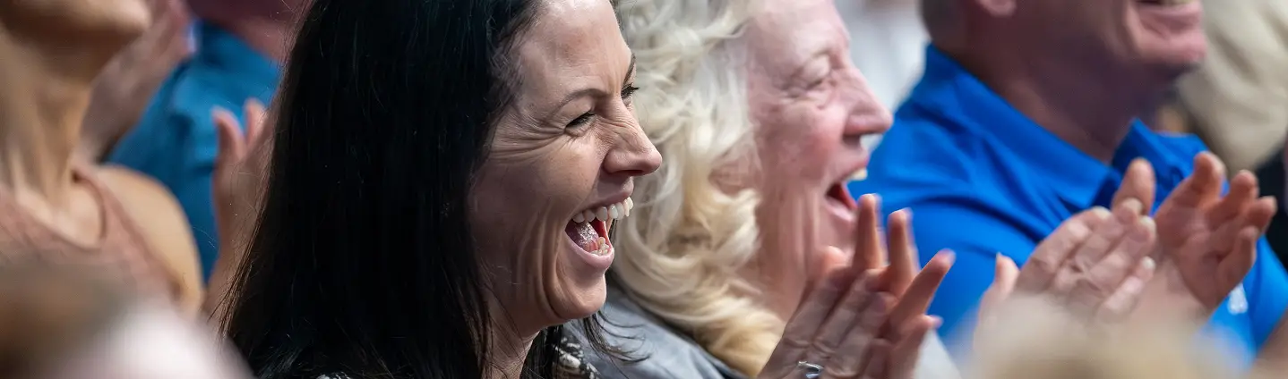 Audience members joyfully laughing and clapping during a live event, capturing a moment of shared happiness and excitement.