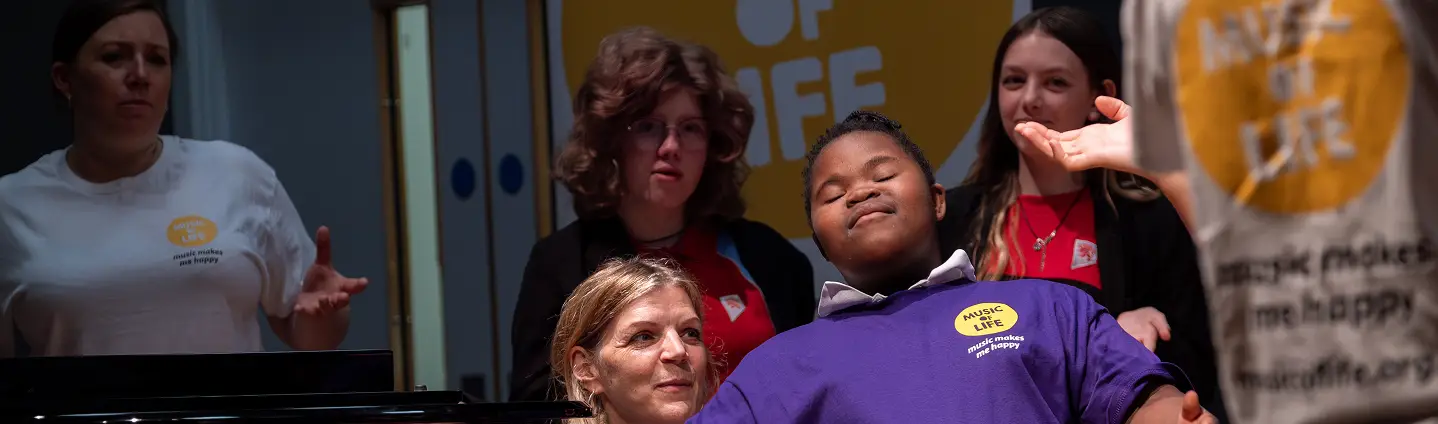 Group of people at a Music of Life event, one in purple shirt joyfully interacting with others on stage.