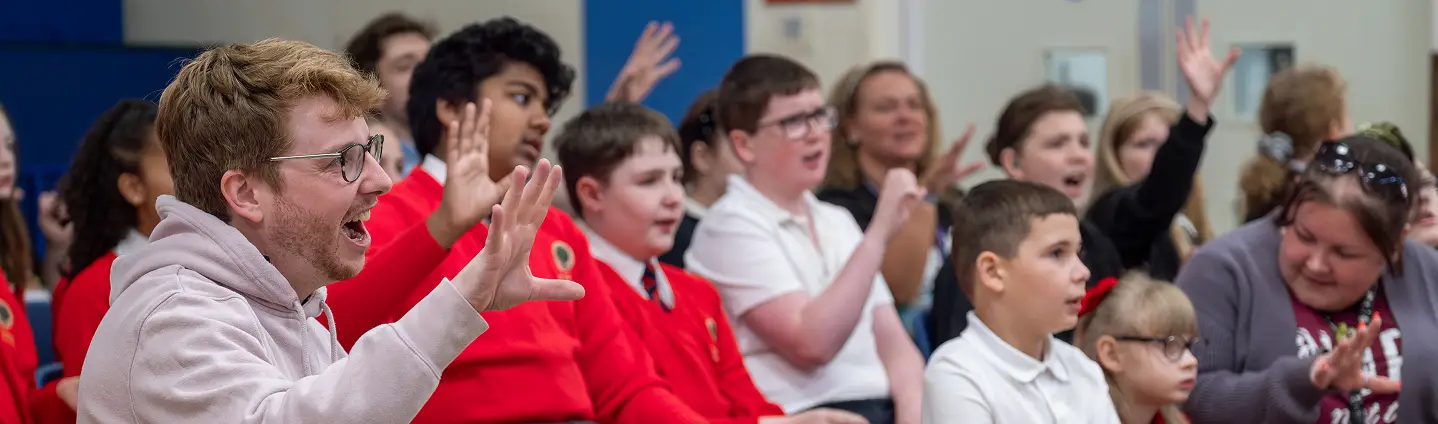Children and adults raising hands and engaging in a lively classroom or event setting.