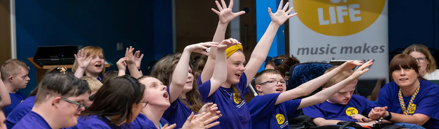 A group of enthusiastic children in purple shirts joyfully participate in a lively music workshop.
