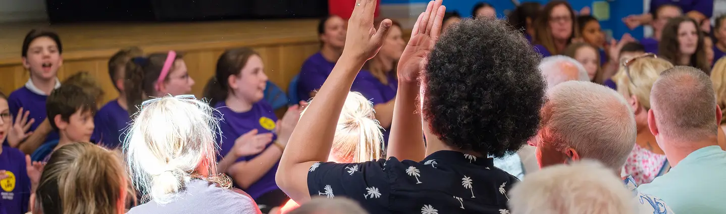 Diverse group of people at a community event, engaging with raised hands and lively discussions.