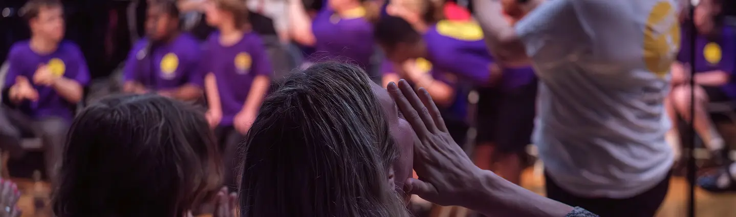 Audience member cheering at a live performance with a group in purple shirts on stage.