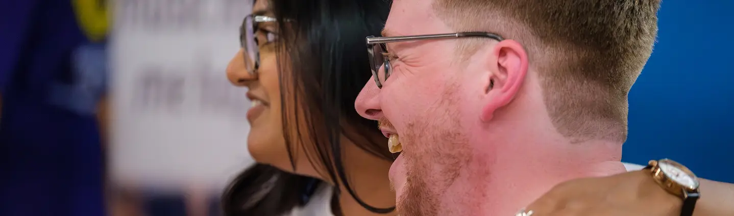 Two friends smiling and embracing, enjoying a joyful moment together indoors.