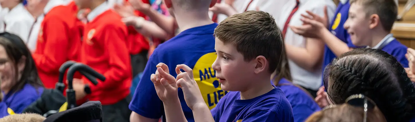Children clapping and engaging in a lively school event, wearing colorful shirts, and creating an inclusive atmosphere.