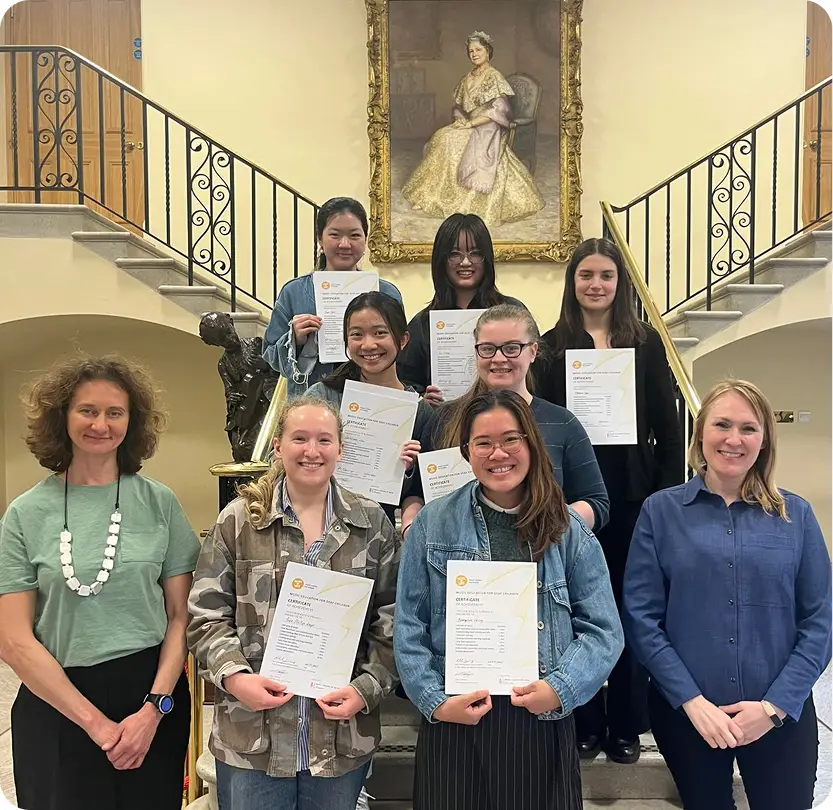 Group of students proudly holding certificates on a staircase, flanked by two teachers.