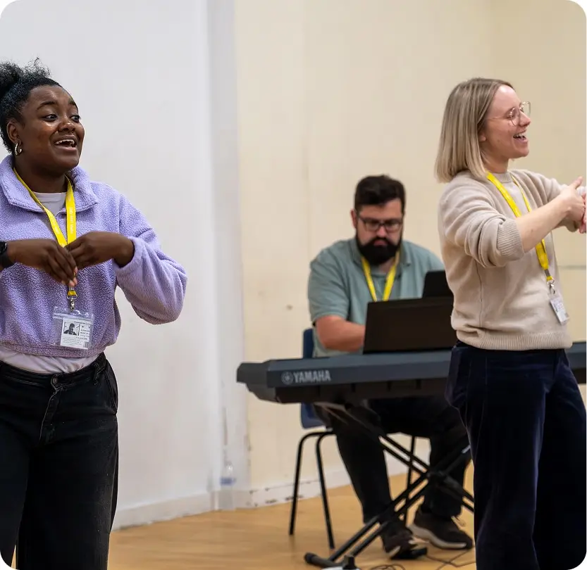People engaging in a lively music session with piano accompaniment, wearing ID badges in a bright room.
