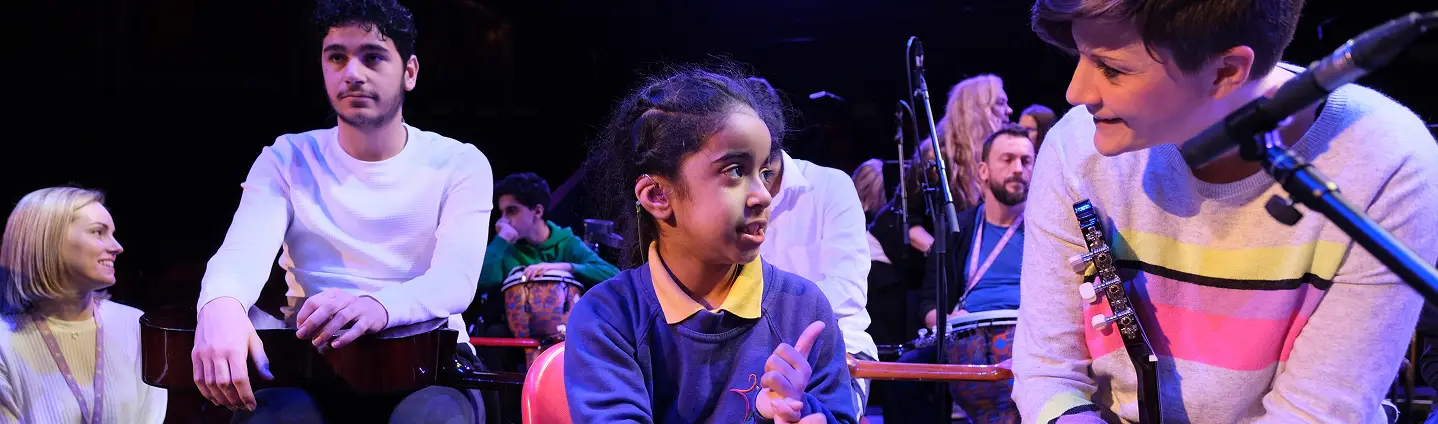 Group of diverse musicians engaging with a young girl on stage, creating an inclusive musical experience.