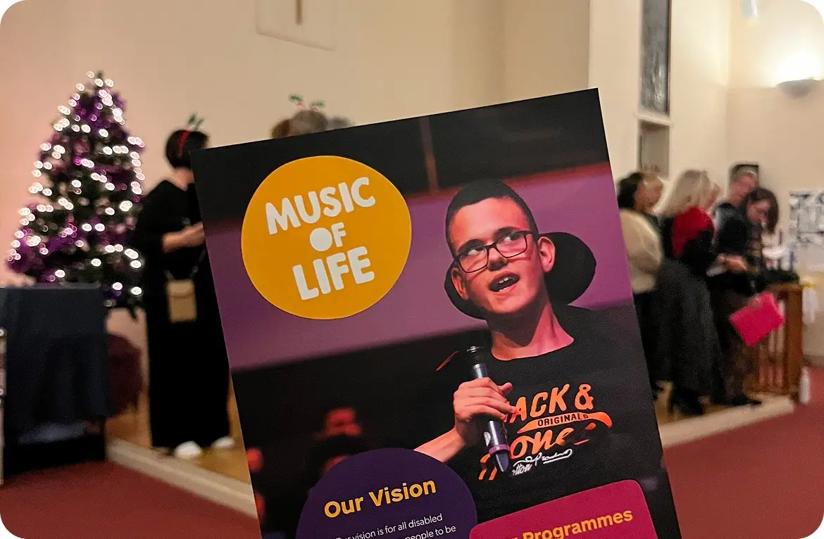 Flyer for Music of Life event with a microphone, Christmas tree, and people in the background.