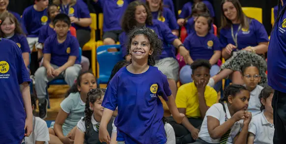 Children enjoying a school event wearing blue and yellow uniforms, with a girl smiling in the foreground.
