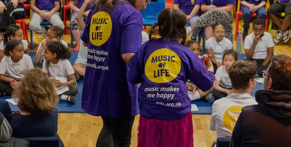 Children and adults participate in a music event wearing Music of Life shirts, highlighting joy and engagement.