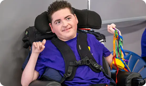 Young person in a wheelchair smiling and holding colorful ribbons, promoting joy and inclusivity in disability awareness.