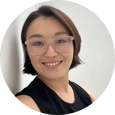 image 64 (1) A person with short hair and glasses smiling at the camera, wearing a black top against a light background.