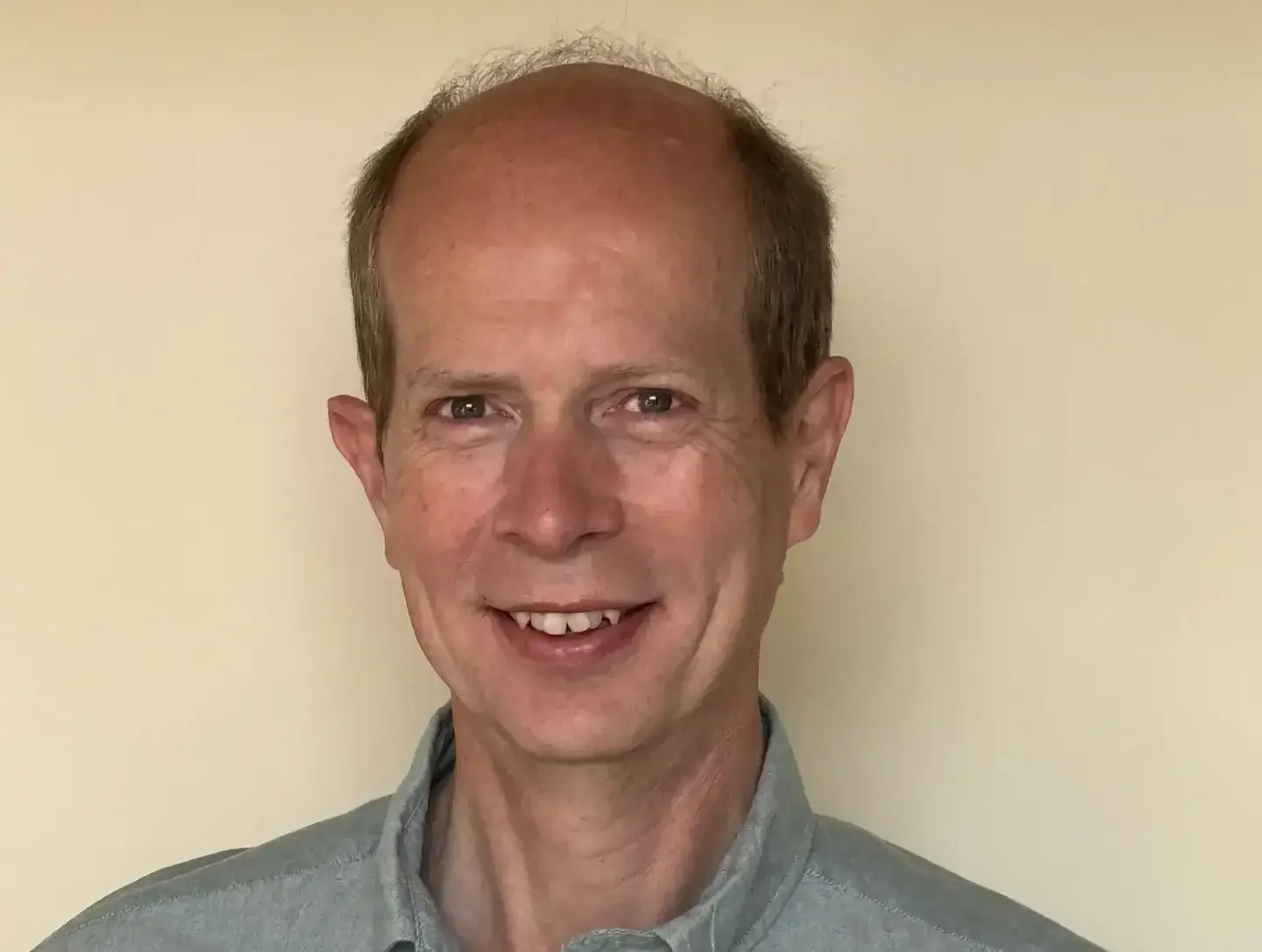 Portrait of a smiling man in a light-colored shirt against a plain background.